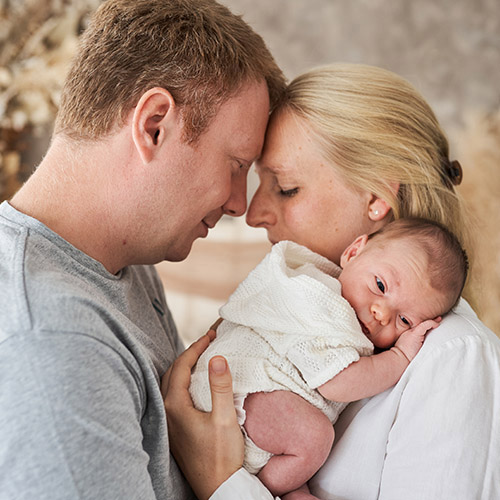 Neugeborenen-Fotoshooting mit Eltern – Baby wird liebevoll von Mutter und Vater im Studio gehalten.