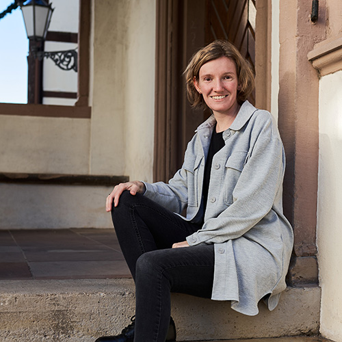 Portrait der Fotografin Annika Rose, die lächelnd auf den Steinstufen des Lemgoer Rathauses sitzt – natürlich, offen und authentisch.