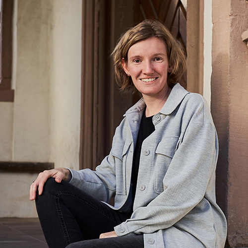 Portrait der Fotografin Annika Rose, die lächelnd auf den Steinstufen des Lemgoer Rathauses sitzt – natürlich, offen und authentisch.